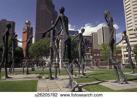 Stock Image -  Calgary, Alberta, Canada, downtown, Family of Man statue stands 21 feet tall with the downtown skyline of Calgary in the province of Alberta.. Fotosearch