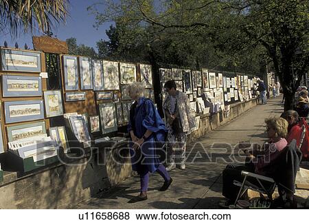 Stock Photo -  Charleston, South Carolina, street art, Tourists walk by displays of artwork for sale on fence in Charleston in the state of South Carolina. . Fotosearch