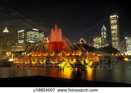 Stock Photo -  Chicago, Illinois, The Buckingham Memorial Fountain at Grant Park is illuminated at night. The illuminated skyline of downtown Chicago towers in the background., . Fotosearch