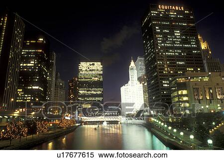 Stock Photography -  Chicago, Illinois, The illuminated skyline of downtown reflects in the waters of the Chicago River at night. The white Wrigley Building is illuminated in the background . Fotosearch