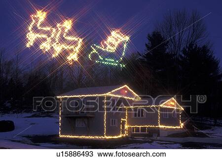 Stock Image -  Christmas, display, decorations, Vermont, House decorated with Christmas lights and reindeer pulling sleigh with Santa Claus illuminated in the sky at night for the holiday season in Washington County in the state of Vermont. . Fotosearch