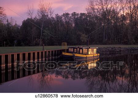 Stock Photo -  Erie Canal, boat, New York, Reflection of a canal boat in the early morning light on the calm waters of the Erie Canal in Rome in the state of New York.. Fotosearch