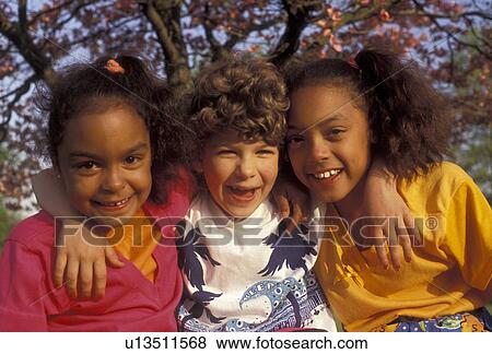 Stock Photo -  friendship, african-american, multi-ethnic, pals, Two (black, African American) girls and one (white, Caucasian) girl with arms around each other and smiling together on a warm spring day in Exton in the state of Pennsylvania. The white girl is in betwee. Fotosearch