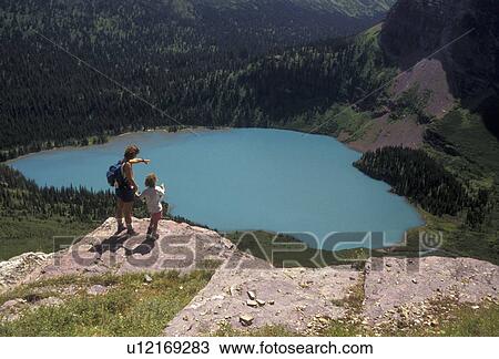 Glacier National Park, Montana, Rocky Mountains, glacier lake, hiking, Waterton-Glacier International Peace Park, Mother and 6 year old daughter stand on overlook above the scenic turquoise colored Grinnell Lake in Glacier National Park in the state of M View Large Photo Image Stock Image - Glacier National Park, Montana, Rocky Mountains, glacier lake, hiking, Waterton-Glacier International Peace Park, Mother and 6 year old daughter stand on overlook above the scenic turquoise colored Grinnell Lake in Glacier National Park in the state of M. Fotosearch