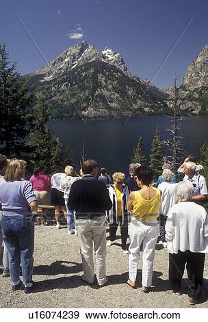 Stock Photo -  Grand Teton National Park, Lake Jenny, Grand Teton, Rocky Mountains, Wyoming, A group of tourists stand at the Lake Jenny overlook to view the scenery of the lake and the majestic Teton mountain range of Grand Teton National Park in the state of Wyoming.. Fotosearch