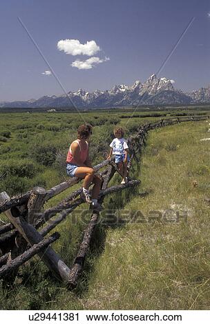 Stock Image -  Grand Teton National Park, mother, daughter, Grand Teton, Rocky Mountains, Grand Teton Mountains, Teton Range, Wyoming, Mother and daughter (6 years old) sit on a buck rail fence at the Cunningham Ranch at the Grand Teton National Park in the state of Wy. Fotosearch