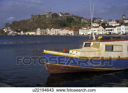 Stock Image -  Grenada, Caribbean, St. George's, Caribbean Islands, Blue and white fishing boat anchored in the calm waters of the harbor with a scenic view of St. George's the capital city on the island of Grenada the spice isle (a British Commonwealth member).. Fotosearch