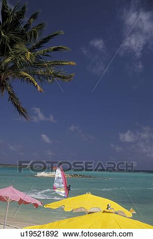Stock Image -  Guadeloupe, Caribbean, resort, Caribbean Islands, Windsurfing on the blue-green water of the Caribbean Sea from the shoreline with yellow and pink beach umbrellas at Hotel Meridien in St. Francois on the island of Grande-Terre in Guadeloupe (a french dep. Fotosearch