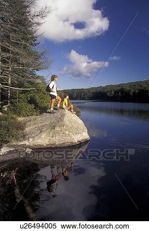 Stock Photography -  hiking, Vermont, Reflection of mother and daughter in the calm waters of Kettle Pond in Groton State Forest in Caledonia County in the state of Vermont. Mother standing on boulder, daughter sitting on boulder. . Fotosearch