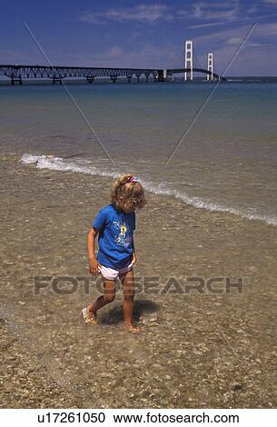 Stock Image -  Lake Michigan, Lake Huron, bridge, Mackinaw City, Michigan, A young girl plays in the shallow water along the shoreline of Lake Huron with a scenic view of Mackinac Bridge Mighty Mac connecting the Lower Peninsula to the Upper Peninsula in Mackinaw City . Fotosearch