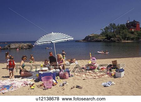 Stock Photo -  Lake Superior, Upper Peninsula, U. P beach, Michigan, People enjoying a day in the sun at Shiras Park Beach with red lighthouse and coast guard station in the distance on Lake Superior in Marquette in the state of Michigan.. Fotosearch