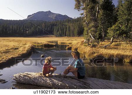 Stock Image -  Lassen Volcanic National Park, Lassen, California, Cascade Mountains, Cascade Range, Mother and daughter (7 years old) sit on a log on Kings Creek in Lassen Volcanic Nat'l Park in the state of California.. Fotosearch