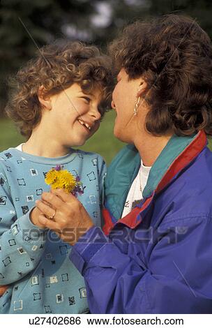Stock Photograph -  love, affection, parenting, Mother and 5 year old daughter embrace and smile at each other as they hold a bouquet of yellow dandelions in their hands. The little girl just brought the flowers to her mother.. Fotosearch