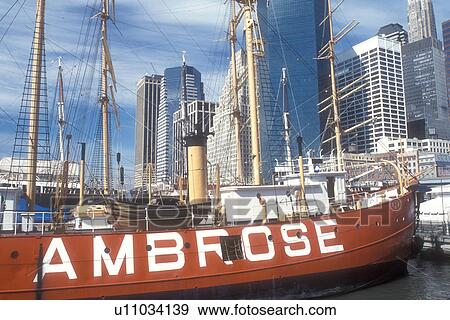 Stock Photo -  Manhattan, New York City, New York, boat, N. Y. C Skyline of Lower Manhattan and South Street Seaport on the East River in New York City, New York. The red 1908 Ambrose vessel moored at the pier.. Fotosearch