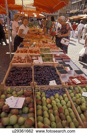 Stock Image -  market, fruit, Switzerland, Lausanne, Vaud, Europe, People shopping at a produce stand with umbrellas at a street market at Place de la Palud in Lausanne in the Canton of Vaud.. Fotosearch