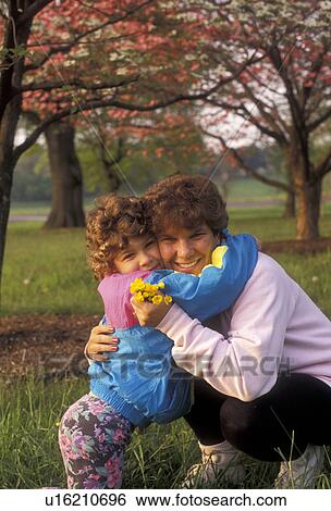 Stock Photograph -  mother, child, hugging, Mother and daughter hugging and smiling after daughter gave her mother some yellow flowers. Mother holding yellow flowers in her hand.. Fotosearch