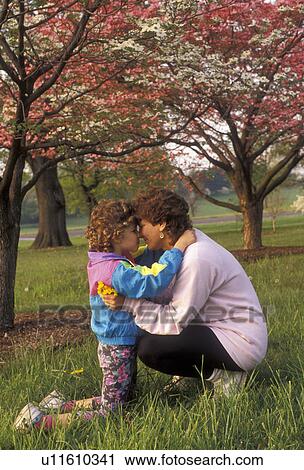 Stock Image -  mother, child, Mother and daughter rubbing noses under pink and white Dogwood trees in a park in the spring. Mother holding yellow flowers in her hand . Fotosearch