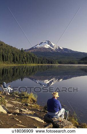 Stock Photo -  Mount Hood, mirror, fishing, Oregon, A senior couple fishes on the shore of Tillium Lake with the snow covered Mt. Hood reflecting in the calm waters in Mount Hood National Forest in the state of Oregon. . Fotosearch
