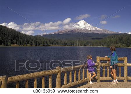 Mount Hood, Oregon, Mother and daughter stand on a wooden deck looking across Tillium Lake at the snow covered Mt. Hood in Mount Hood National Forest in the state of Oregon., View Large Photo Image Stock Photo - Mount Hood, Oregon, Mother and daughter stand on a wooden deck looking across Tillium Lake at the snow covered Mt. Hood in Mount Hood National Forest in the state of Oregon., . Fotosearch
