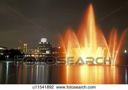 Stock Image -  Nebraska, The colorful illuminated Heartland of America Fountain reflects in the water at the Heartland of America Park in Omaha at night.. Fotosearch