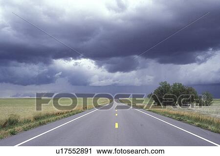 Stock Image -  Nebraska, The storm clouds hover overhead as Highway 20 stretches for miles into the distant horizon.. Fotosearch