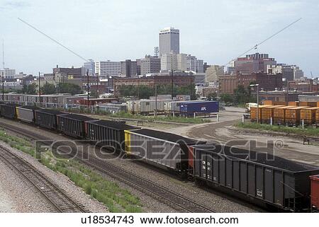 Stock Image -  Nebraska, Train carrying coal at train depot in Omaha. Skyline of downtown Omaha.. Fotosearch