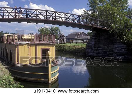 Stock Image -  New York, Rome, The Erie Canal Village. An 1840 restored community. Canal tour boat docked on the side of the canal . Fotosearch