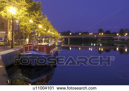 Stock Image -  New York, Seneca Falls, Finger Lakes, A cruise line boat along Cayuga-Seneca Canal reflects in the calm evening water.. Fotosearch