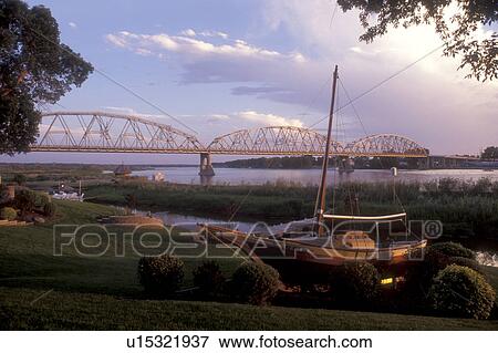 North Dakota, Bismarck, A sailboat is beached on the shoreline of the Missouri River in the early evening in Bismarck. A bridge spans the river in the background View Large Photo Image Stock Photo - North Dakota, Bismarck, A sailboat is beached on the shoreline of the Missouri River in the early evening in Bismarck. A bridge spans the river in the background . Fotosearch