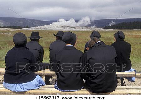 Stock Photo -  Old Faithful, Yellowstone National Park, geyser, amish, Wyoming, Yellowstone, A group of Amish sit on benches waiting to watch The Old Faithful Geyser erupt in Yellowstone National Park in the state of Wyoming. . Fotosearch