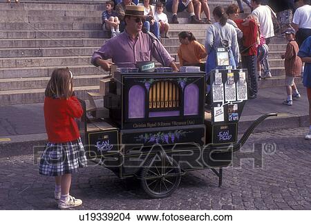 Picture -  Paris, France, Europe, Montmartre, music, A street musician plays an old fashioned music box on the steps of the Basilique du Sacre Coeur in Montmartre while a young Parisian girl listens.. Fotosearch