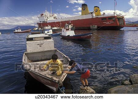 Patagonia, Chile, Pacific Ocean, Two boys play on a fishing boat in the harbor as a passenger/cargo ferry boat is docked in Puerto Natales in Chile. View Large Photo Image Stock Photo - Patagonia, Chile, Pacific Ocean, Two boys play on a fishing boat in the harbor as a passenger/cargo ferry boat is docked in Puerto Natales in Chile. . Fotosearch