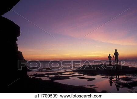 Stock Photo -  Pictured Rocks, Lake Superior, silhouette, sunset, sunrise, Upper Peninsula, U. P Michigan, Mother and daughter standing holding hands on the edge of Lake Superior at sunset at Pictured Rocks National Lakeshore in Munising in the state of Michigan.. Fotosearch