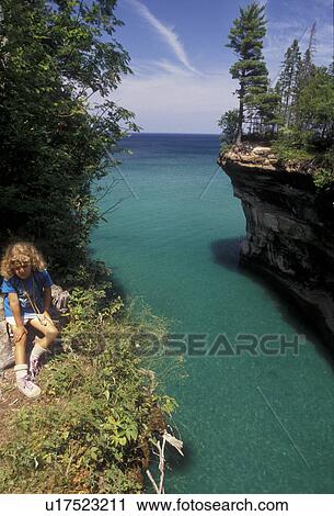 Pictured Rocks, Lake Superior, Upper Peninsula, U. P Michigan, Young girl sits next to sandstone cliffs along the coast of Lake Superior at Pictured Rocks National Lakeshore in Munising in the state of Michigan. View Large Photo Image Stock Image - Pictured Rocks, Lake Superior, Upper Peninsula, U. P Michigan, Young girl sits next to sandstone cliffs along the coast of Lake Superior at Pictured Rocks National Lakeshore in Munising in the state of Michigan.. Fotosearch