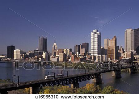 Pittsburgh, skyline, Pennsylvania, A scenic view of the downtown skyline of Pittsburgh from across the Monongahela River in the state of Pennsylvania. A public train crosses a bridge over the river heading away from the city. View Large Photo Image Stock Image - Pittsburgh, skyline, Pennsylvania, A scenic view of the downtown skyline of Pittsburgh from across the Monongahela River in the state of Pennsylvania. A public train crosses a bridge over the river heading away from the city. . Fotosearch