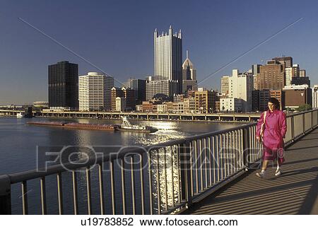 Pittsburgh, skyline, Pennsylvania, A woman wearing a pink coat walks across Smithfield Street Bridge which crosses the Monongahela River with a view of the downtown skyline of Pittsburgh behind in the state of Pennsylvania. A barge cruises slowly down th View Large Photo Image Stock Image - Pittsburgh, skyline, Pennsylvania, A woman wearing a pink coat walks across Smithfield Street Bridge which crosses the Monongahela River with a view of the downtown skyline of Pittsburgh behind in the state of Pennsylvania. A barge cruises slowly down th. Fotosearch