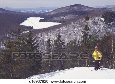 Stock Image -  snowshoeing, Vermont, VT, Woman snowshoeing on Owl's Head overlooking the frozen Kettle Pond in Groton State Forest in winter.. Fotosearch