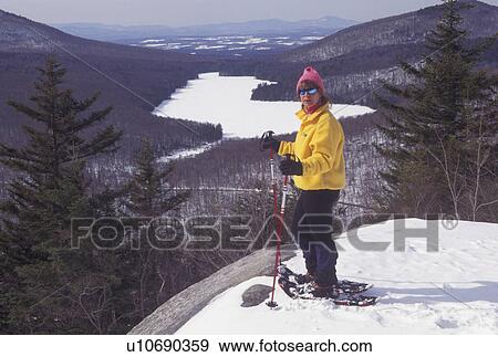 Stock Photo -  snowshoeing, Vermont, VT, Woman snowshoeing on Owl's Head overlooking the frozen Kettle Pond in Groton State Forest in winter.. Fotosearch