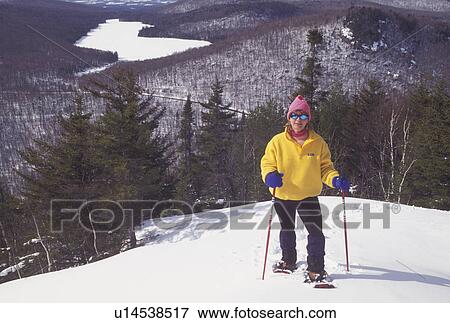 Stock Photo -  snowshoeing, Vermont, VT, Woman snowshoeing on Owl's Head overlooking the frozen Kettle Pond in Groton State Forest in winter.. Fotosearch