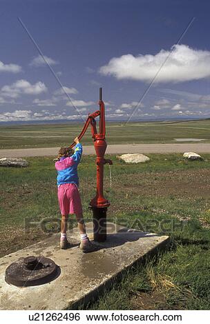 Stock Photograph -  South Dakota, Geographical Center of United States, Belle Fourche, water pump, A young girl pumps water from a red water pump at the Geographical Center of the United States in Belle Fourche in the state of South Dakota. . Fotosearch