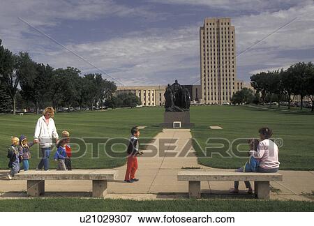 Stock Photo -  State Capitol, Bismarck, State House, North Dakota, Women and children in the foreground with the State Capitol Building skyscraper of the prairie in the distance in the capital city of Bismarck in the state of North Dakota.. Fotosearch