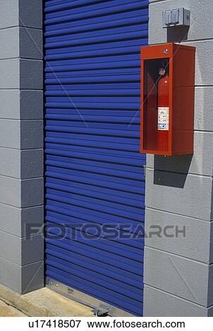Stock Photo -  storage unit, A red fire extinquisher hangs on the wall next to a blue door of storage unit.. Fotosearch