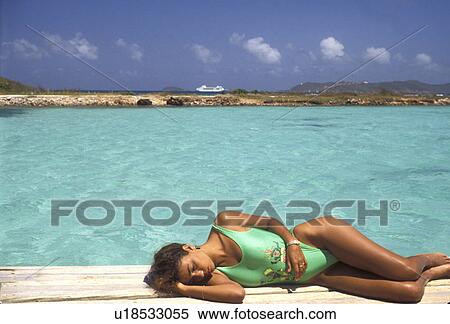 Stock Photography -  sunbathing, Caribbean, Union Island, Grenadine Islands, Caribbean Islands, Woman in green bathing suit sunbathing next to the green waters of the Caribbean Sea on Union Island in the St. Vincent Grenadines (a British Commonwealth member).. Fotosearch