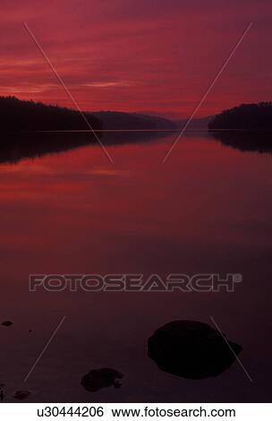 Stock Photograph -  sunrise, sunset, reflection, lake, Blue Ridge Mountains, Virginia, The orange/red sky reflects in the calm waters of Philpott Reservoir/Lake at sunrise in the state of Virginia.. Fotosearch