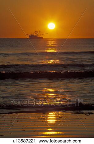 Stock Image -  sunrise, sunset, shrimp boat, Cumberland Island, Georgia, A shrimp boat passes along the horizon as the sun rises on Sea Camp Beach from Cumberland Island National Seashore.. Fotosearch