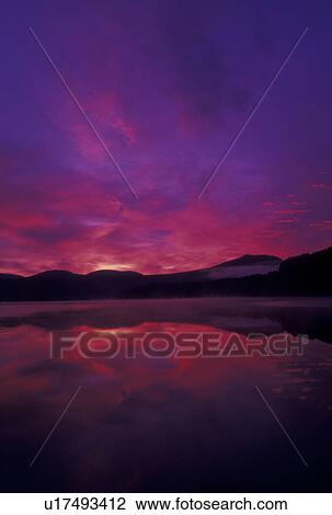 Stock Image -  sunrise, sunset, Vermont, The beautiful red and purple sky reflects in the calm waters of Molly Falls Pond at sunrise in Marshfield in Washington County in the state of Vermont. . Fotosearch