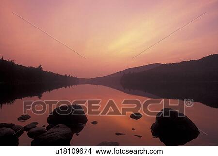 sunset, lake, Vermont, The orange sky reflects in the calm waters of Kettle Pond at sunset with boulders in the foreground in Groton State Forest in Caledonia County in the state of Vermont. View Large Photo Image Picture - sunset, lake, Vermont, The orange sky reflects in the calm waters of Kettle Pond at sunset with boulders in the foreground in Groton State Forest in Caledonia County in the state of Vermont. . Fotosearch
