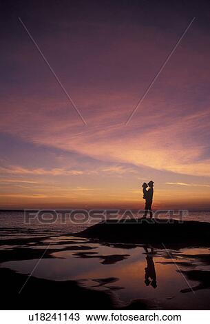 Stock Image -  sunset, sunrise, silhouette, Lake Superior, Pictured Rocks, Upper Peninsula, U. P Michigan, Mother and daughter standing on the edge of Lake Superior at sunset at Pictured Rocks National Lakeshore in Munising in the state of Michigan.. Fotosearch