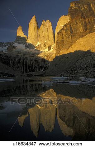Stock Photo -  Torres del Paine National Park, Chile, Andes, Patagonia, The sun shines golden on the huge granite pillar rock formations of the Torres (tower) Del Paine Mountains which reflect in the calm lake in Parque Nacional Torres Del Paine (National Park) in Chil. Fotosearch