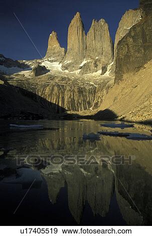 Torres del Paine National Park, Patagonia, Chile, Andes, The sun shines on the huge granite pillar rock formations of the Torres (tower) Del Paine Mountains which reflect in the calm lake in Parque Nacional Torres Del Paine (National Park) in Chile. View Large Photo Image Stock Photo -  Torres del Paine National Park, Patagonia, Chile, Andes, The sun shines on the huge granite pillar rock formations of the Torres (tower) Del Paine Mountains which reflect in the calm lake in Parque Nacional Torres Del Paine (National Park) in Chile.. Fotosearch